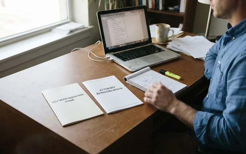 A person comparing two folders on a desk, one labeled self-represented and the other labeled with an attorney's case file